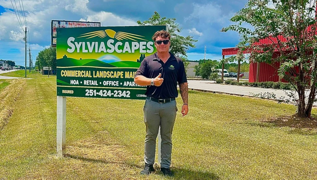 Sylvia Scapes crew member giving a thumbs-up in front of the company commercial landscaping sign
