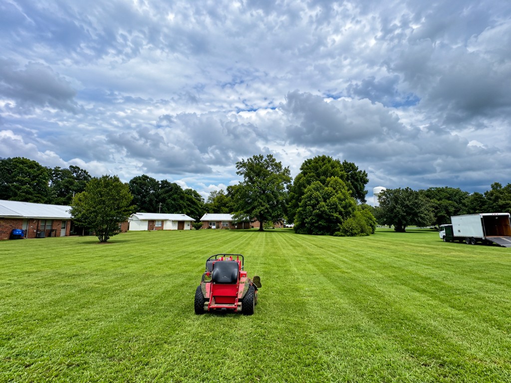 Commercial zero-turn mower on a freshly striped lawn with service truck on site